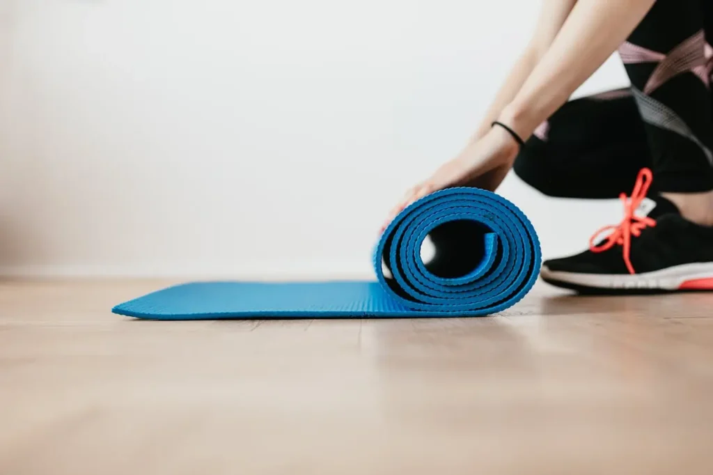 Pilates-en suelo Primer plano de una mujer preparándose para un entrenamiento en interiores enrollando un Mat azul para practicar pilates en labranza .